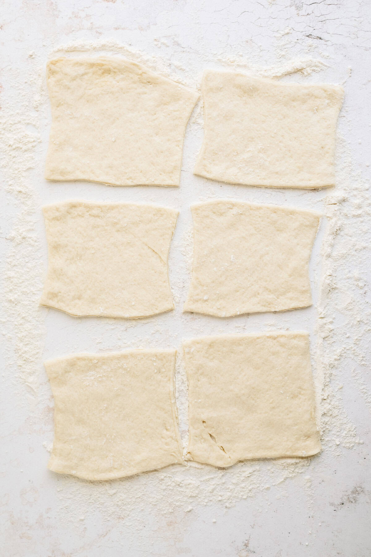 Six rectangular pieces of raw dough are laid out on a floured white surface, evenly spaced in two columns and three rows.