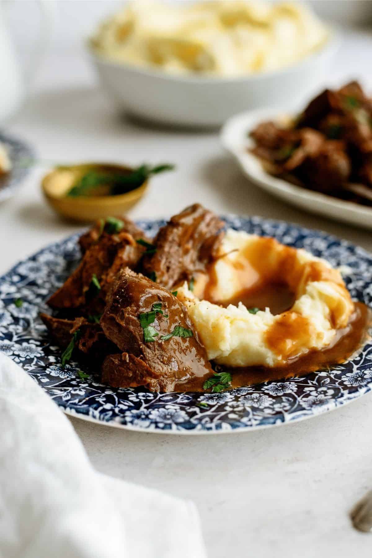 Delicious pot roast served with mashed potatoes and gravy on a blue patterned plate.
