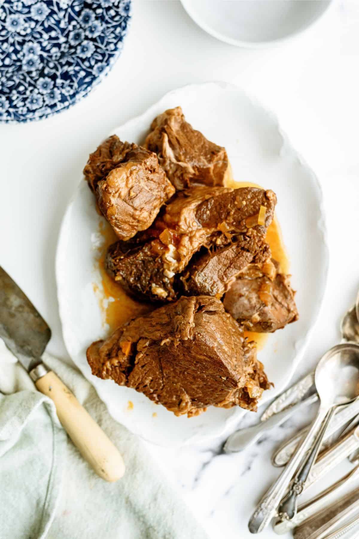 Tender, flavorful pot roast served on a white platter with utensils.