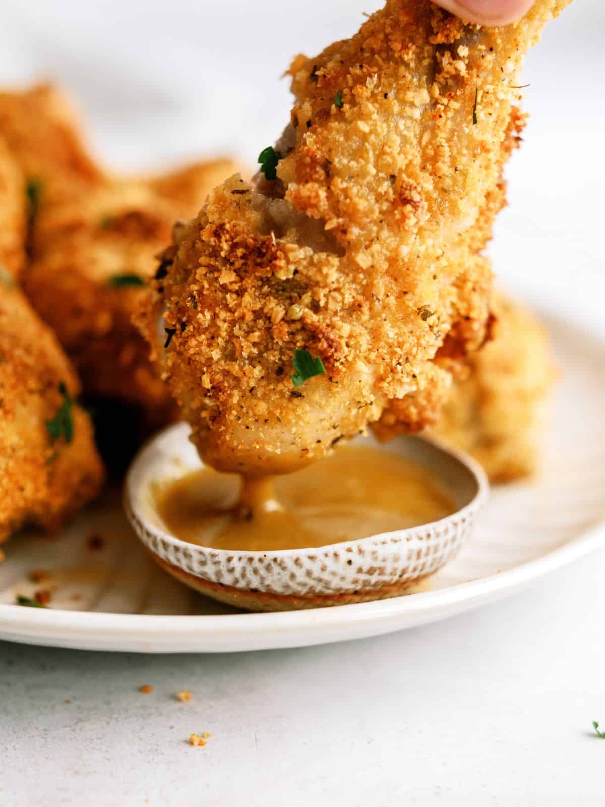 Oven-Fried Parmesan Chicken Drumstick being dipped into honey mustard sauce