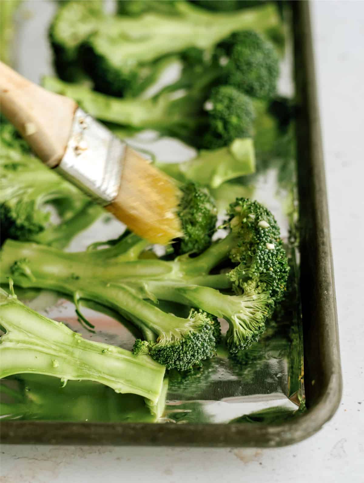 Pastry brush brushing broccoli with olive oil mixture