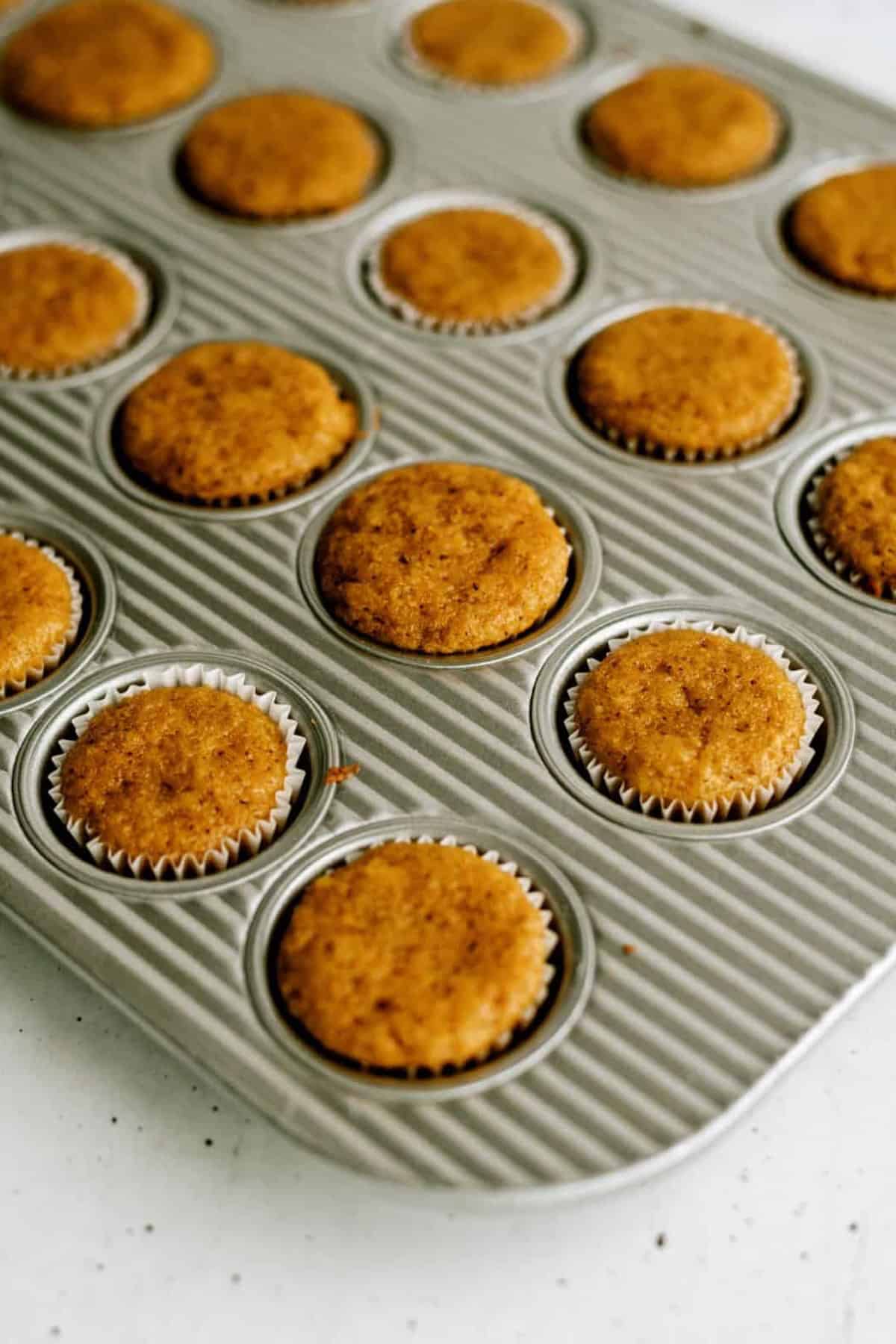 A muffin tray filled with evenly baked, golden-brown muffins placed on a light-colored surface.
