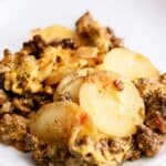 Close-up of a casserole dish containing layers of sliced potatoes, ground meat, and a cheese topping.