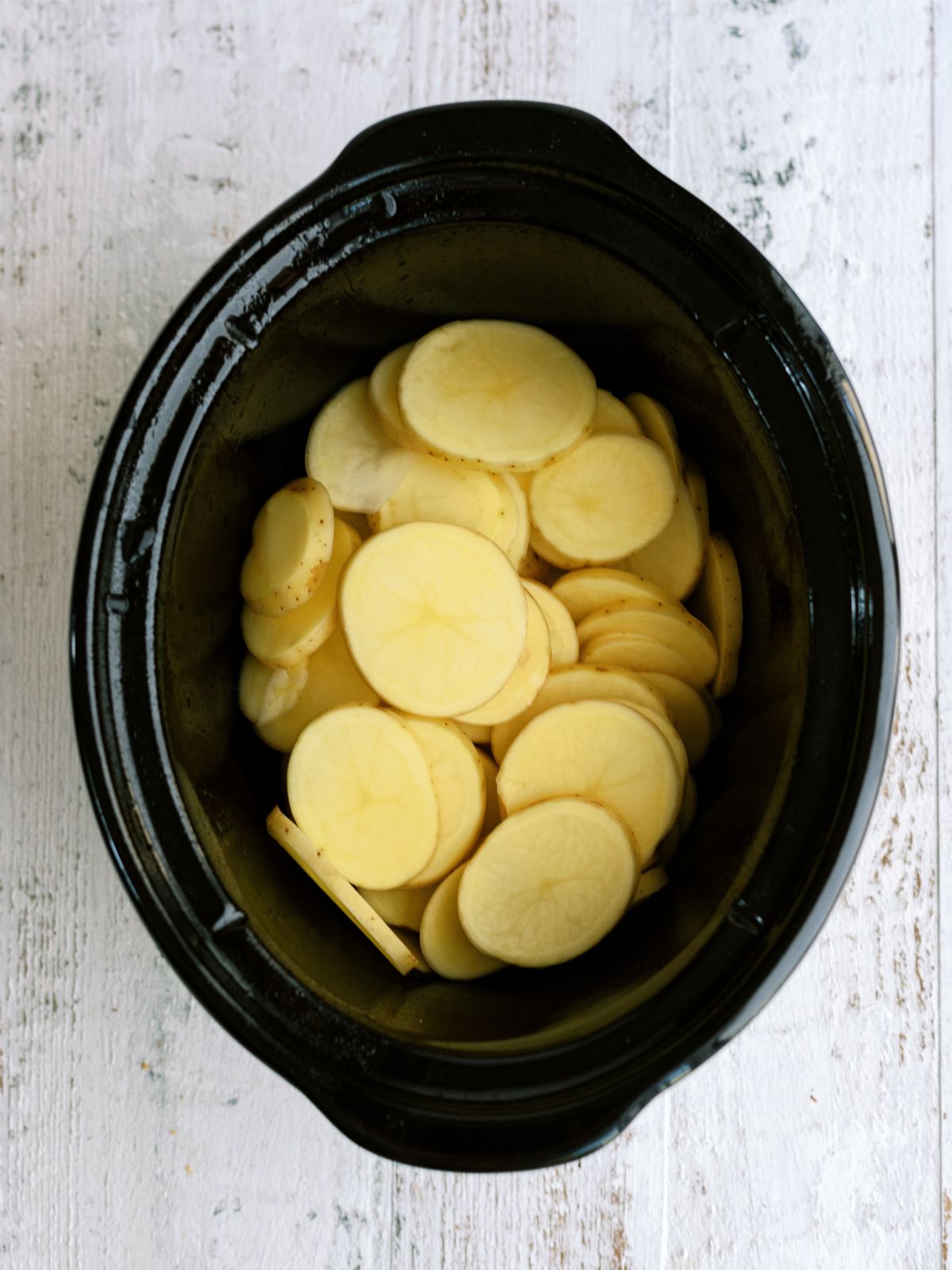 Sliced potatoes in the bottom of slow cooker