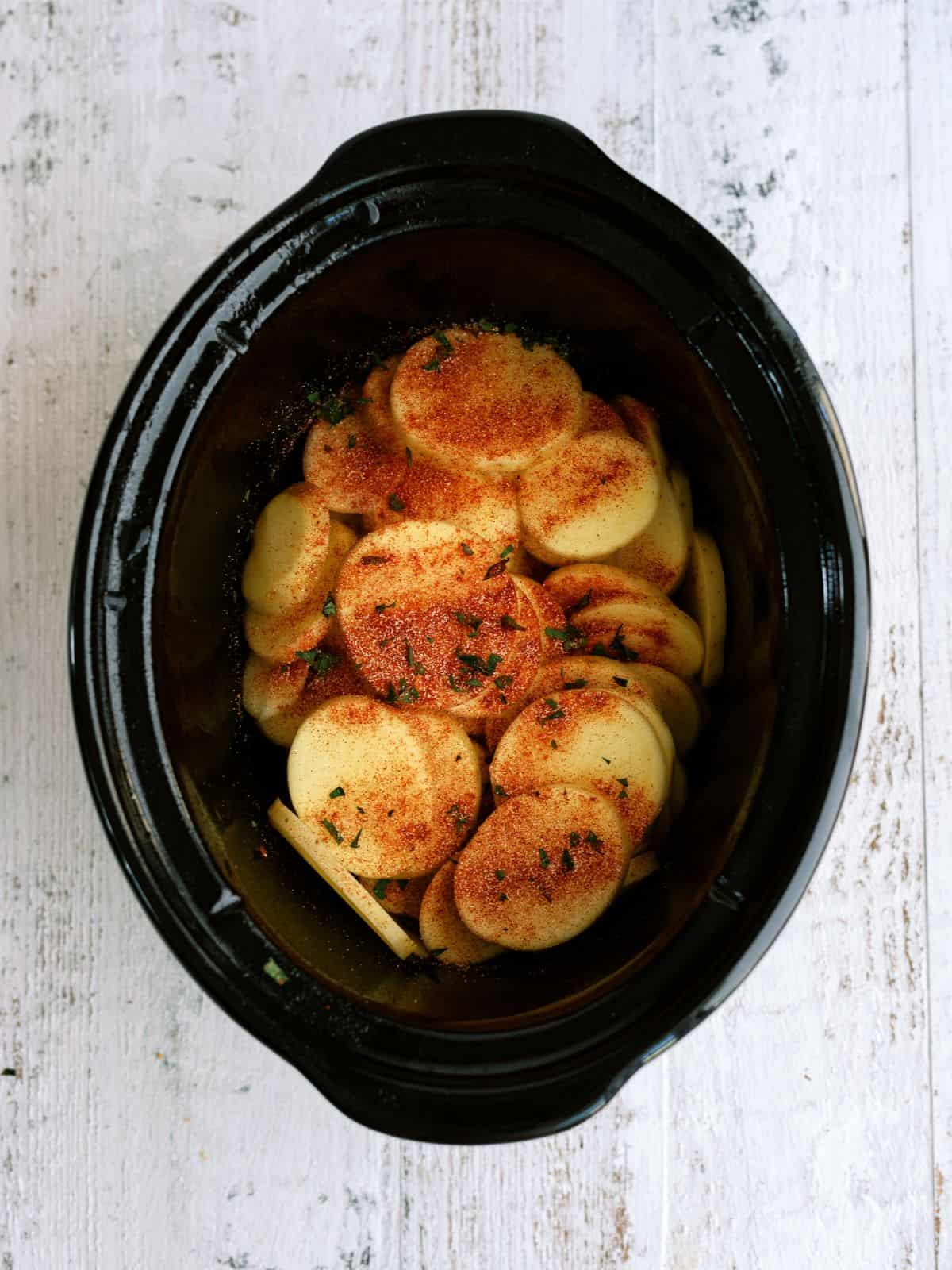 Seasoning on top of sliced potatoes in slow cooker