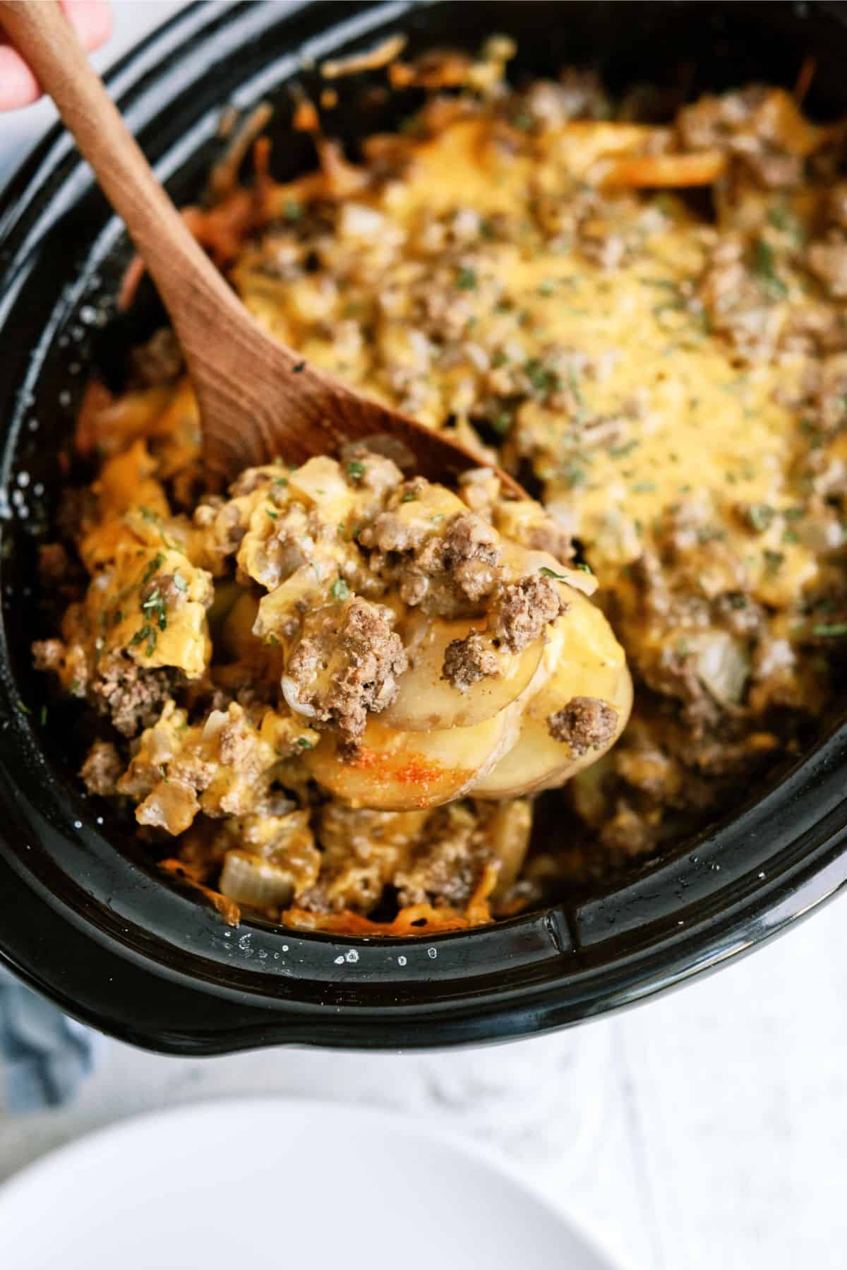 Slow Cooker Cheesy Beef and Potatoes in the slow cooker with a wooden spoon