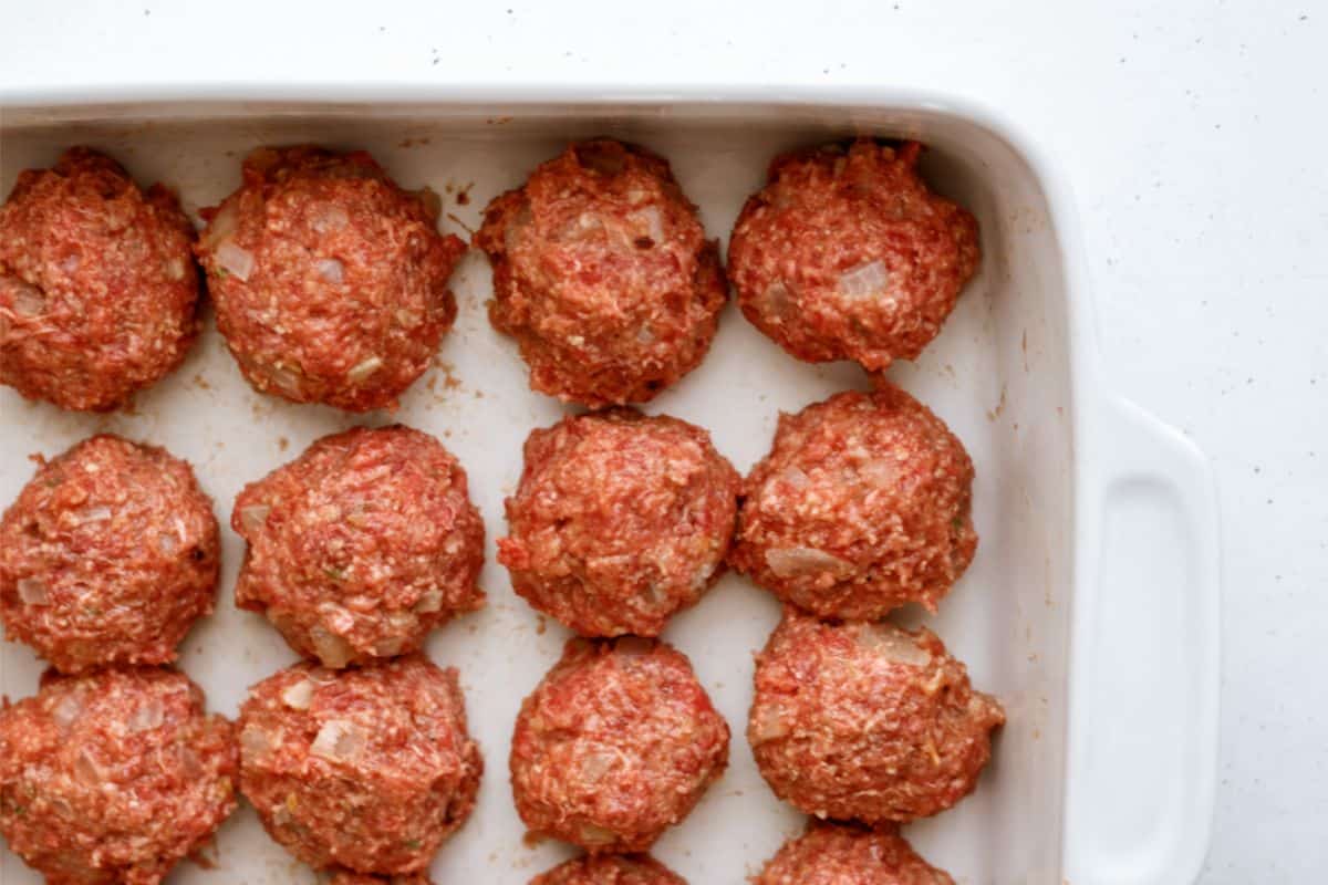 Raw meatballs arranged in rows in a white rectangular baking dish.
