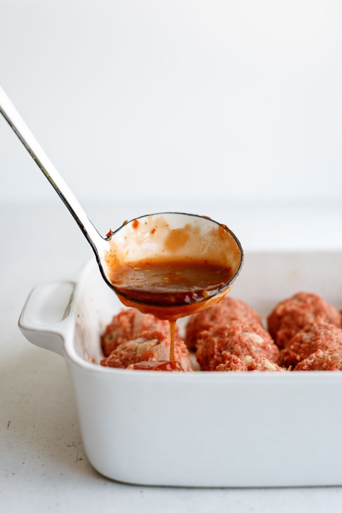 Spooning jelly sauce over meatballs in baking dish