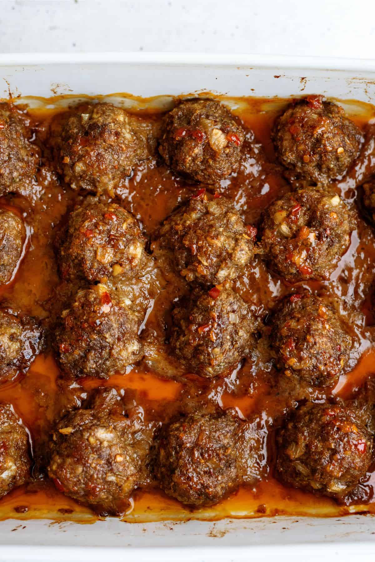 A baking dish filled with evenly spaced, cooked meatballs in a thick, reddish-brown sauce.