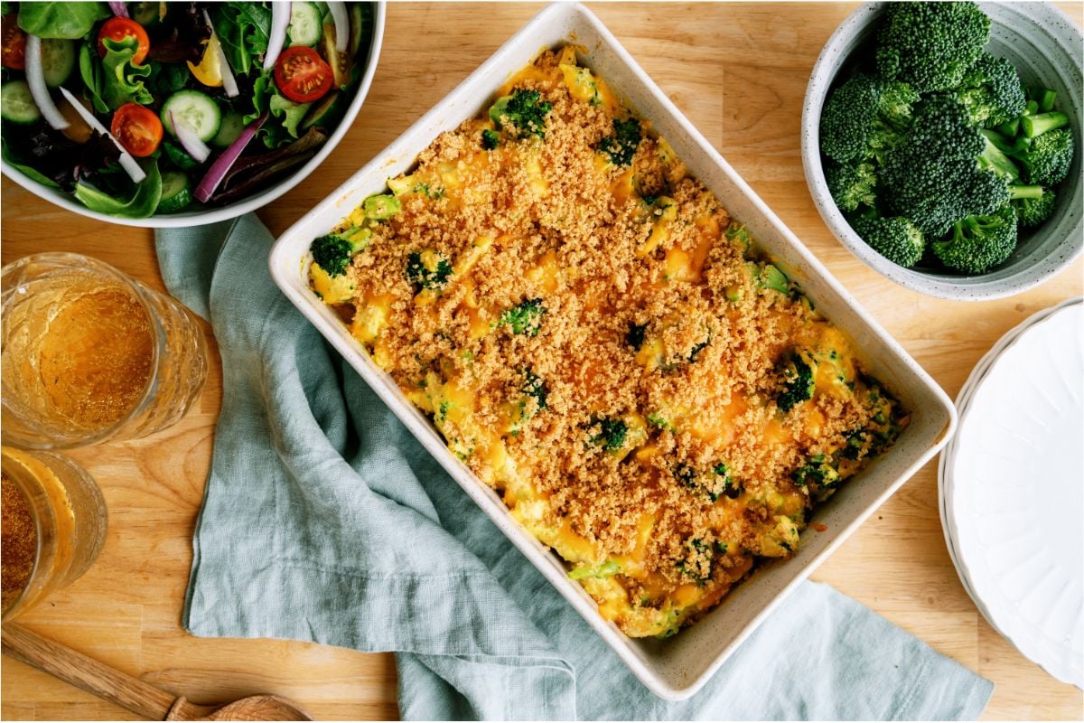 Top view of Chicken and Broccoli Casserole in casserole dish with a salad in the background and a bowl of fresh broccoli.