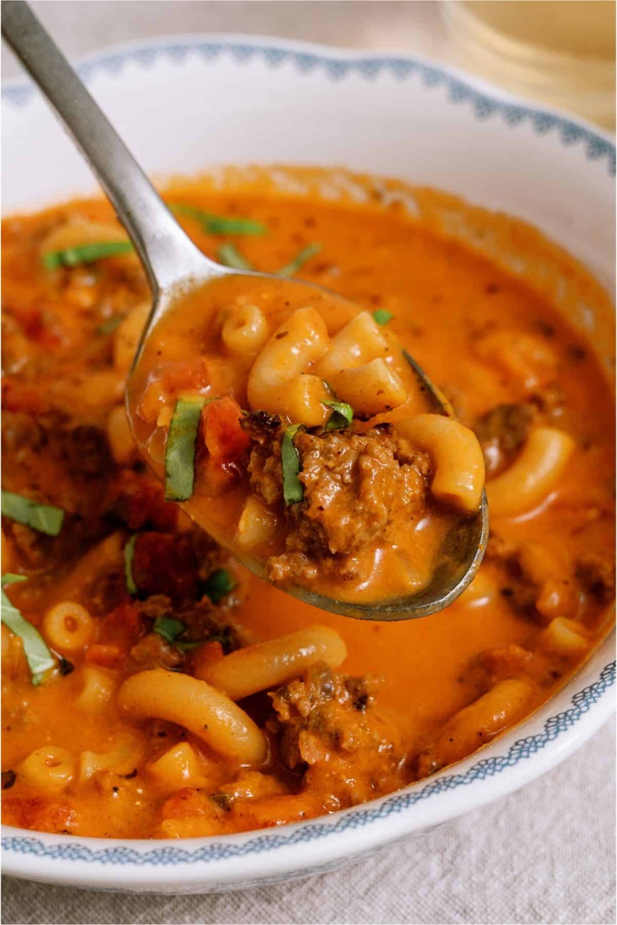 A spoon lifting a bite out of a bowl of Creamy Ground Beef and Tomato Macaroni Soup.