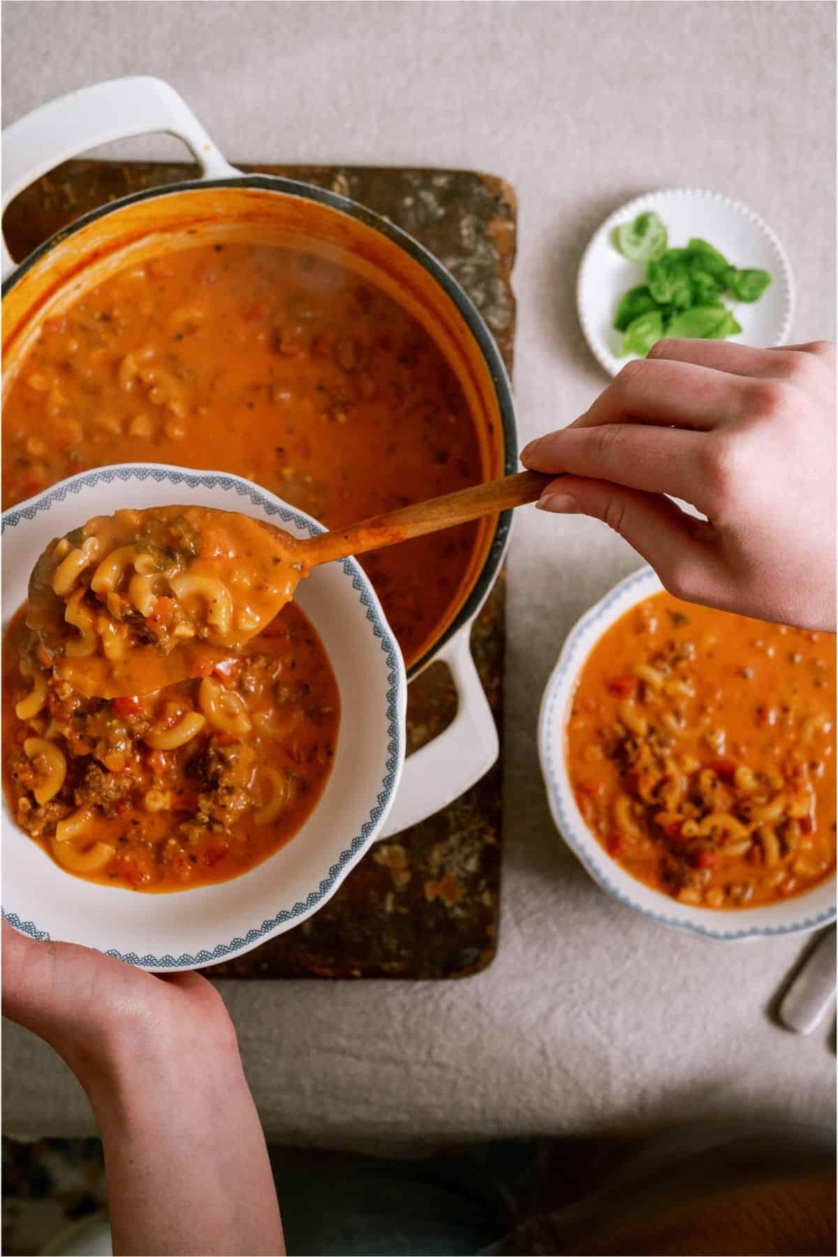Dishing up a bowl of Creamy Ground Beef and Tomato Macaroni Soup out of a large pot.
