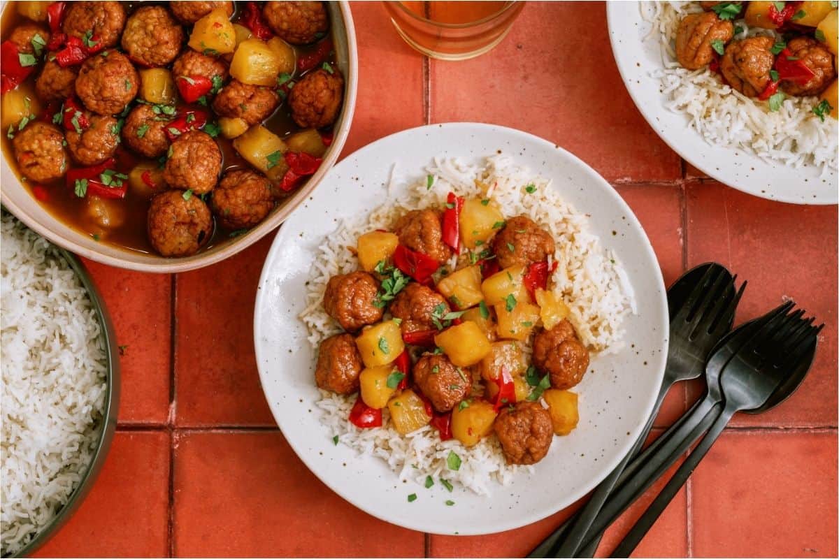 A serving of Instant Pot Hawaiian Meatballs over rice with the remaining Instant Pot Hawaiian Meatballs in a dish.