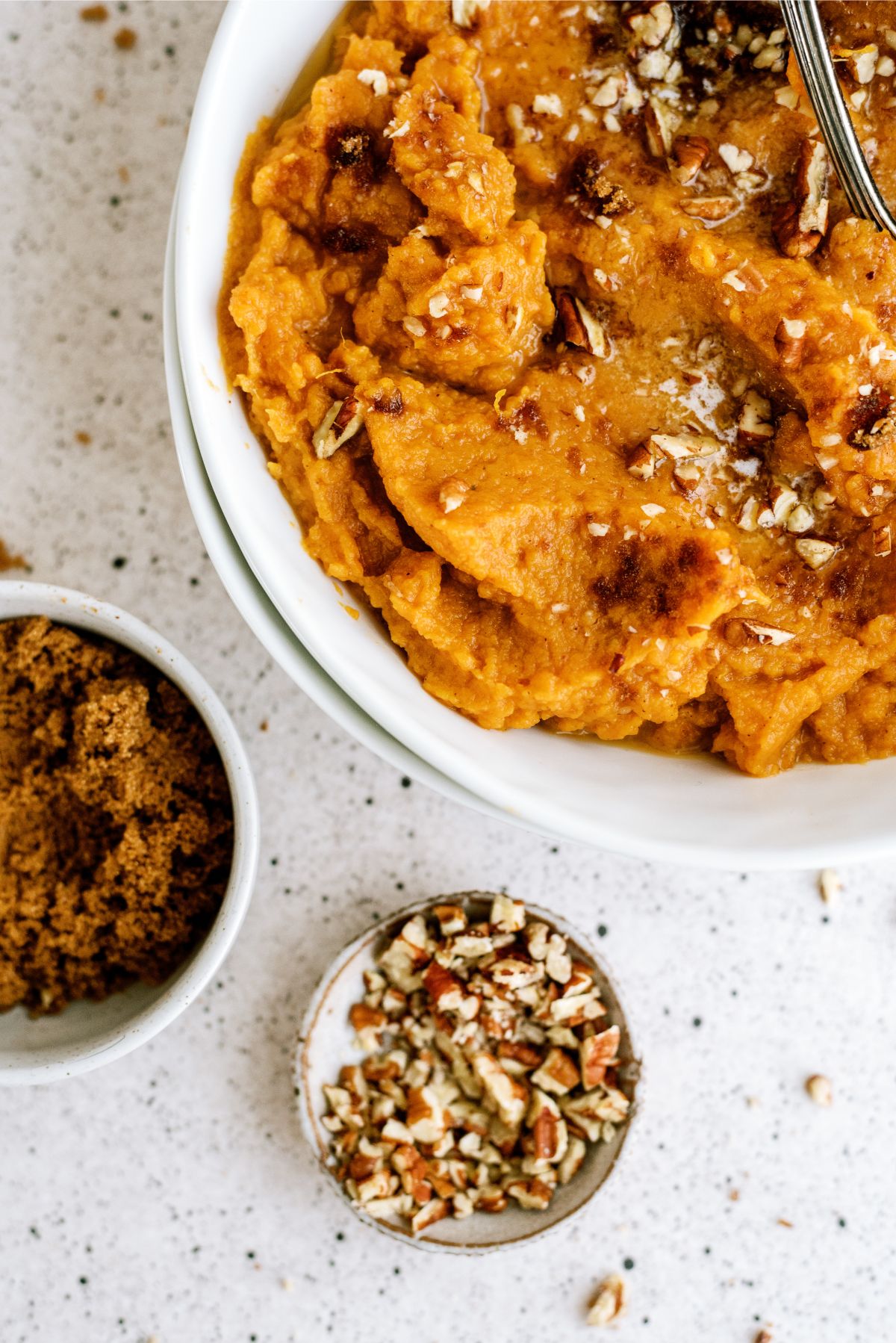 A bowl of Mashed Sweet Potatoes with small bowls of brown sugar and pecans