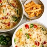 Two bowls of creamy soup topped with sliced jalapeños, tomatoes, crumbled cheese, and tortilla strips, with extra jalapeños and tortilla strips in small bowls nearby.