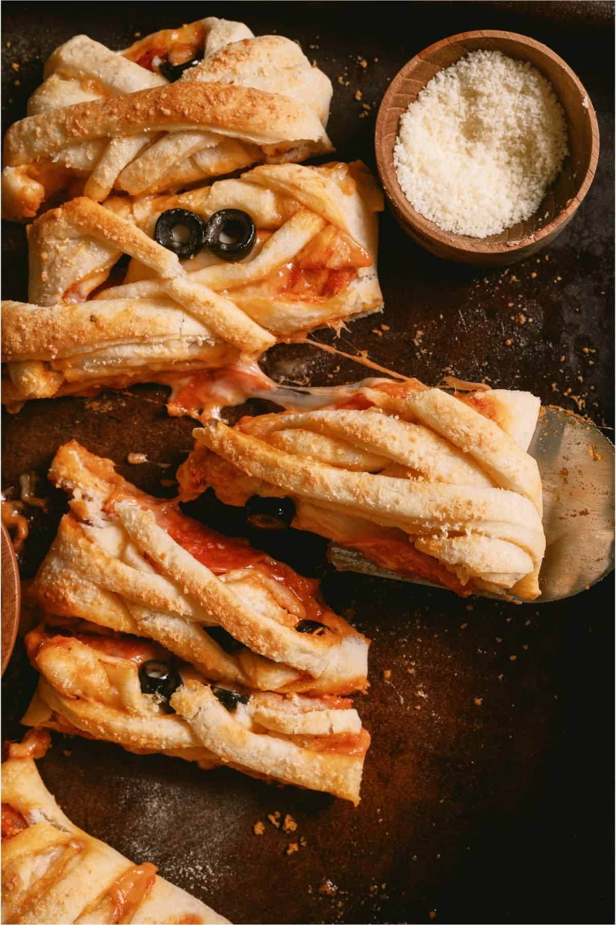 Mummy Pizza Braid cut into slices with a small bowl of parmesan cheese.
