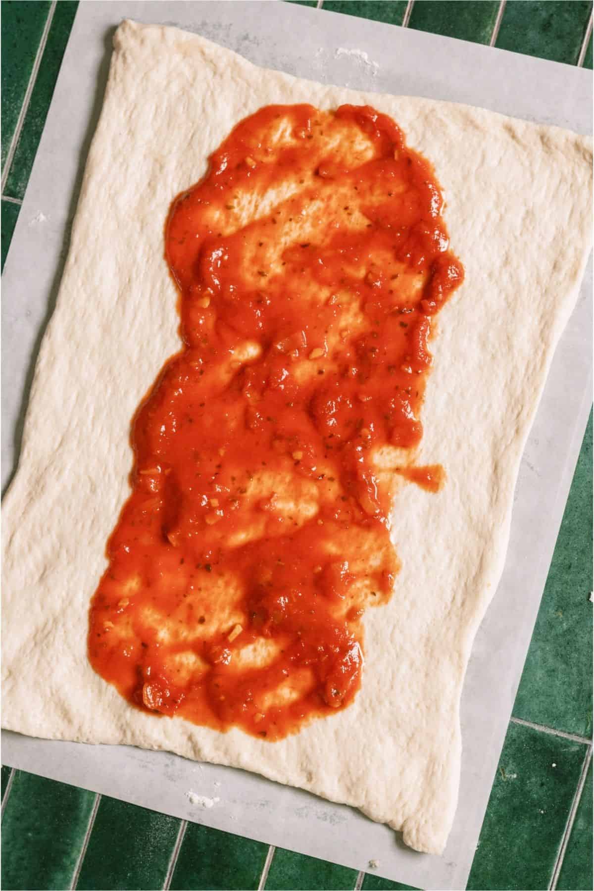 Pizza dough on a pan with sauce spread down the middle.
