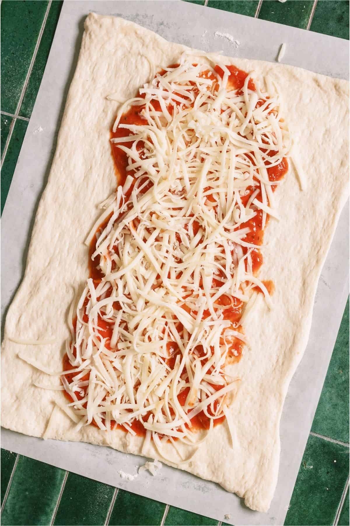 Shredded cheese on top of sauce on pizza dough.