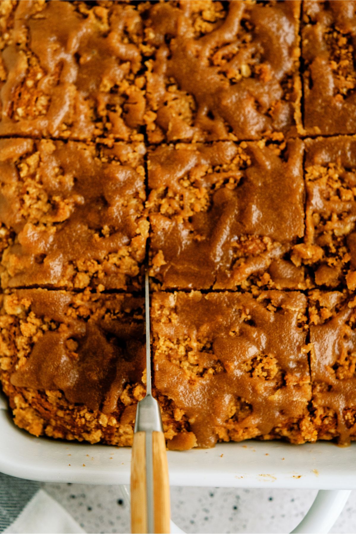 A pan of Pumpkin Coffee Cake with Brown Sugar Glaze with a knife slicing it into squares