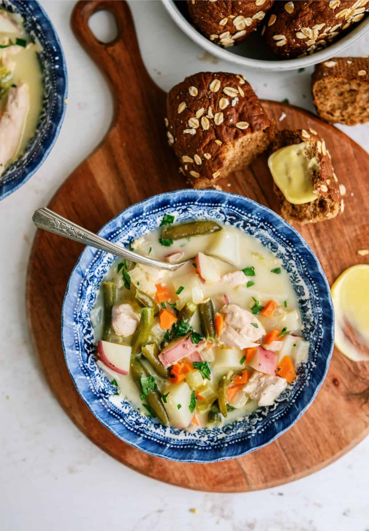 Slow Cooker Creamy Chicken Stew in a bowl with bread on a cutting board