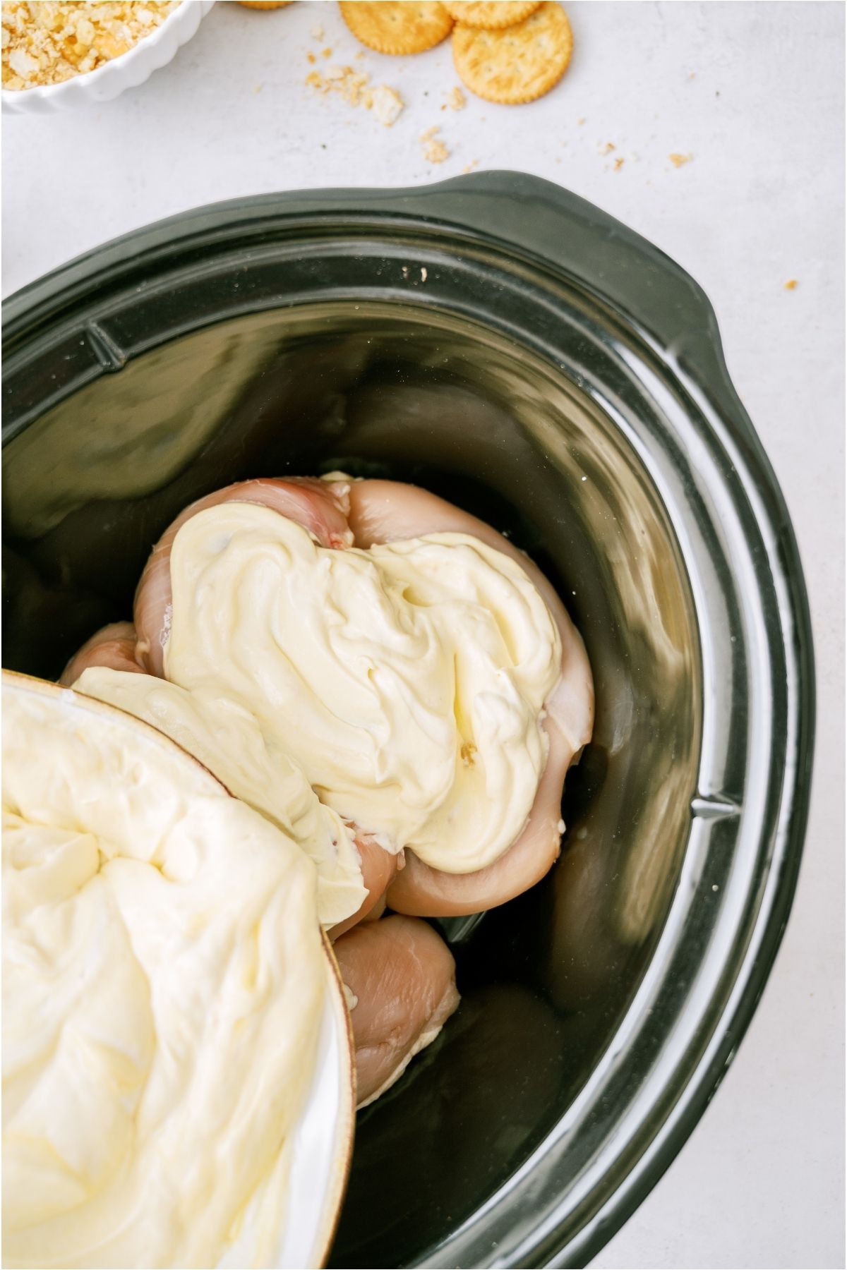 A slow cooker with chicken breasts on the bottom and the soup mixture being poured on top.