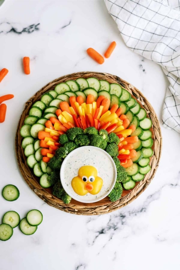 A platter arranged to resemble a turkey, made from sliced cucumbers, carrots, bell peppers, broccoli, and a dip in the center with a small duck decoration.