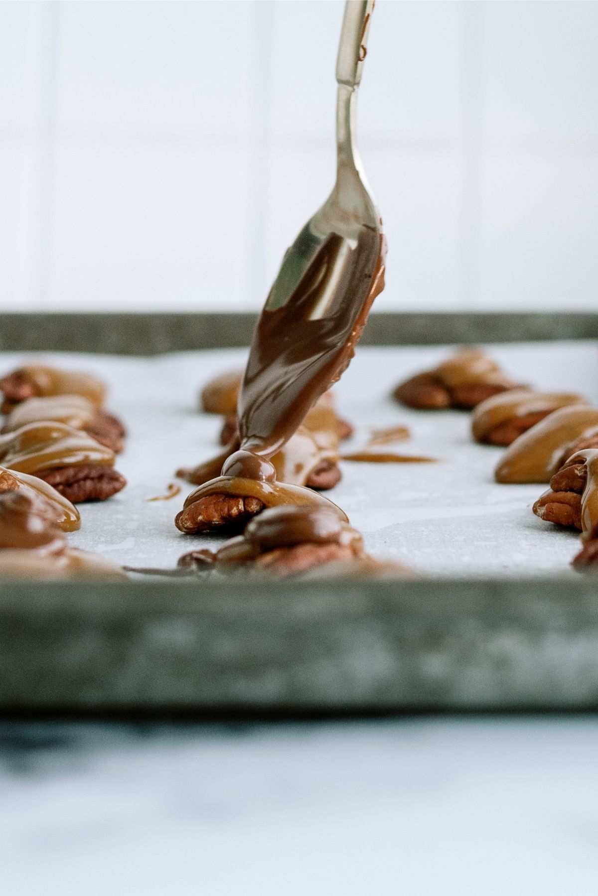 Spooning melted chocolate on top of the caramel pecans