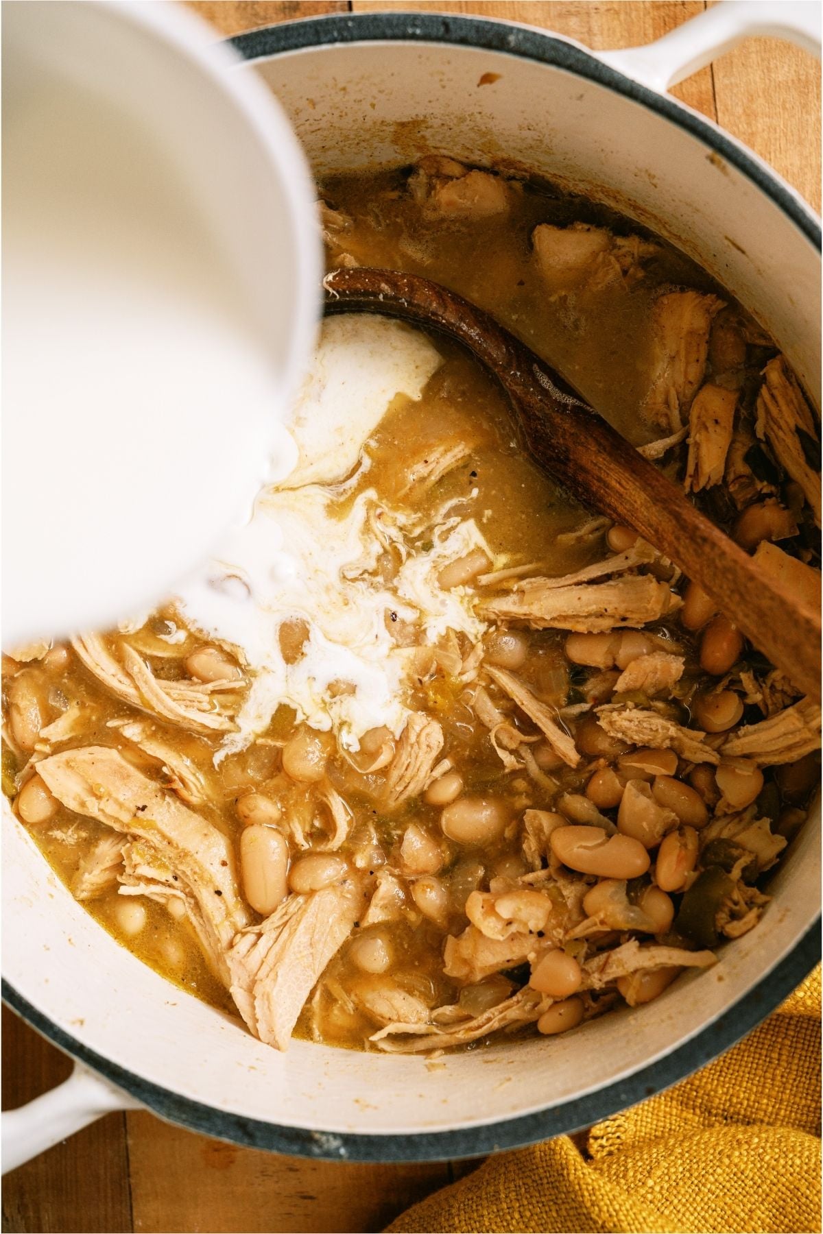 Adding cream to Creamy White Chicken Chili on the stove top.