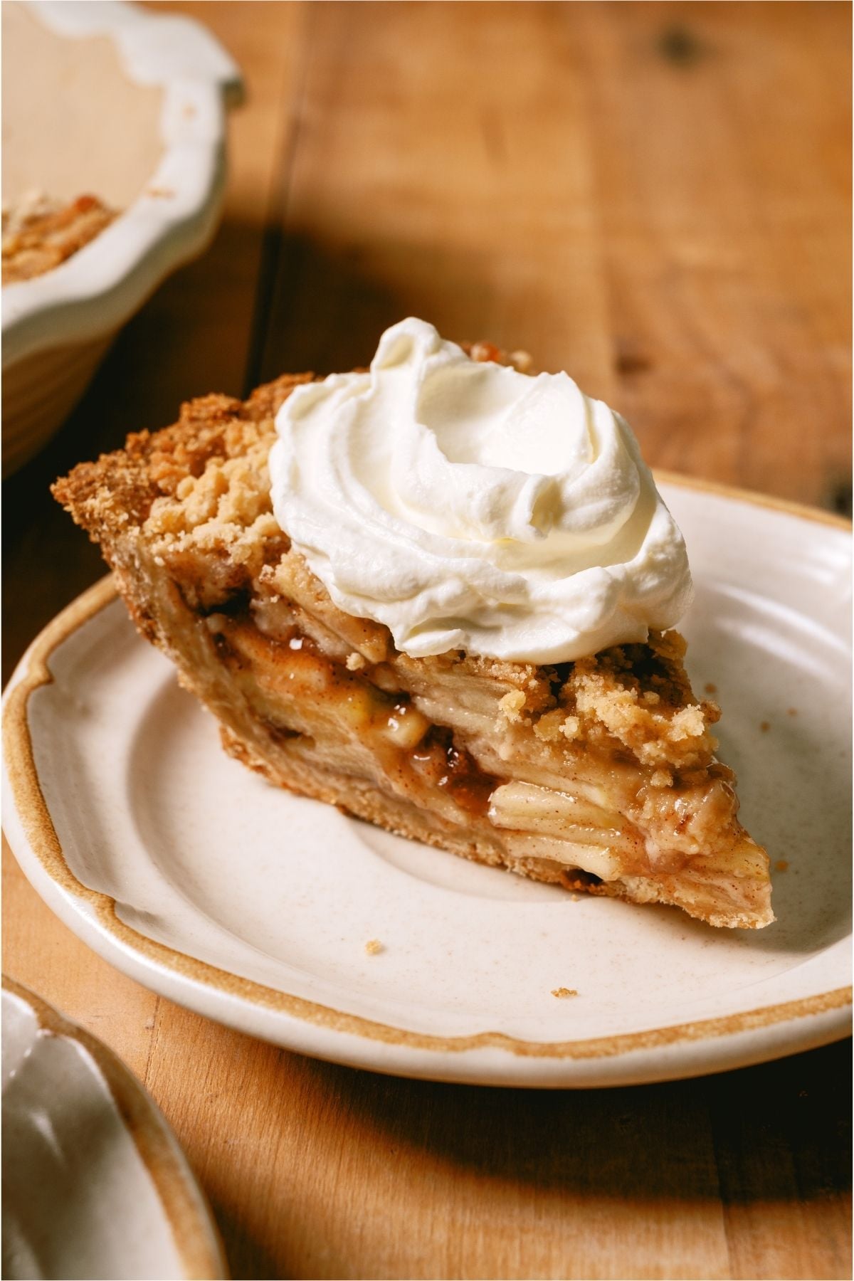 A slice of Dutch Apple Pie on a plate topped with whip cream.