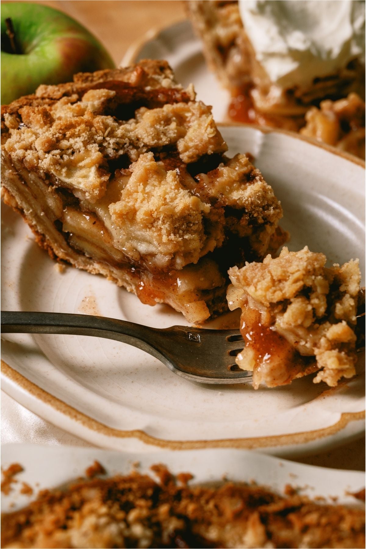 A slice of Dutch Apple Pie on a plate with a fork cutting a bite of it.