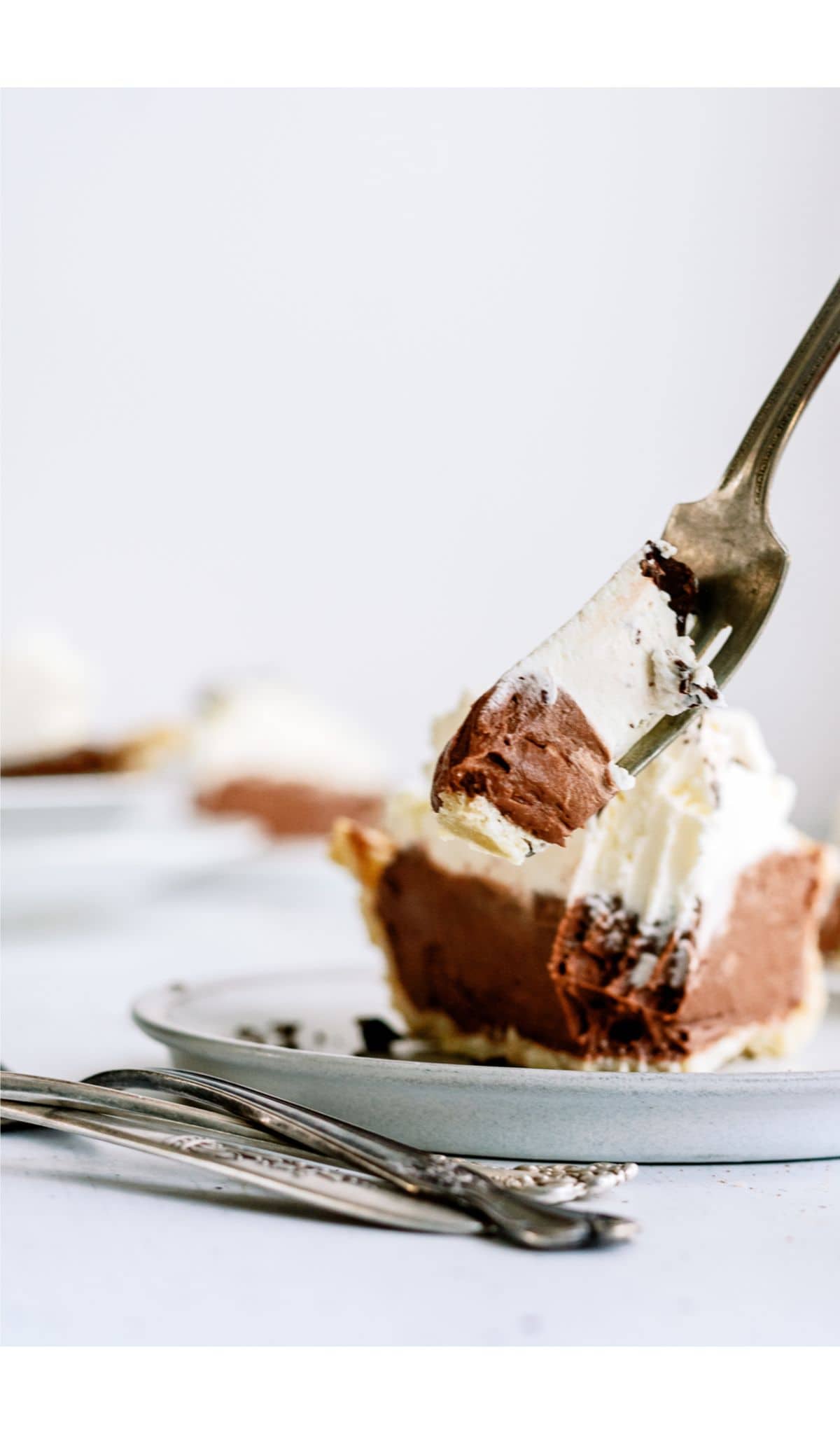 A slice of Chocolate Cream Pie on a plate with a fork lifting a bite off.