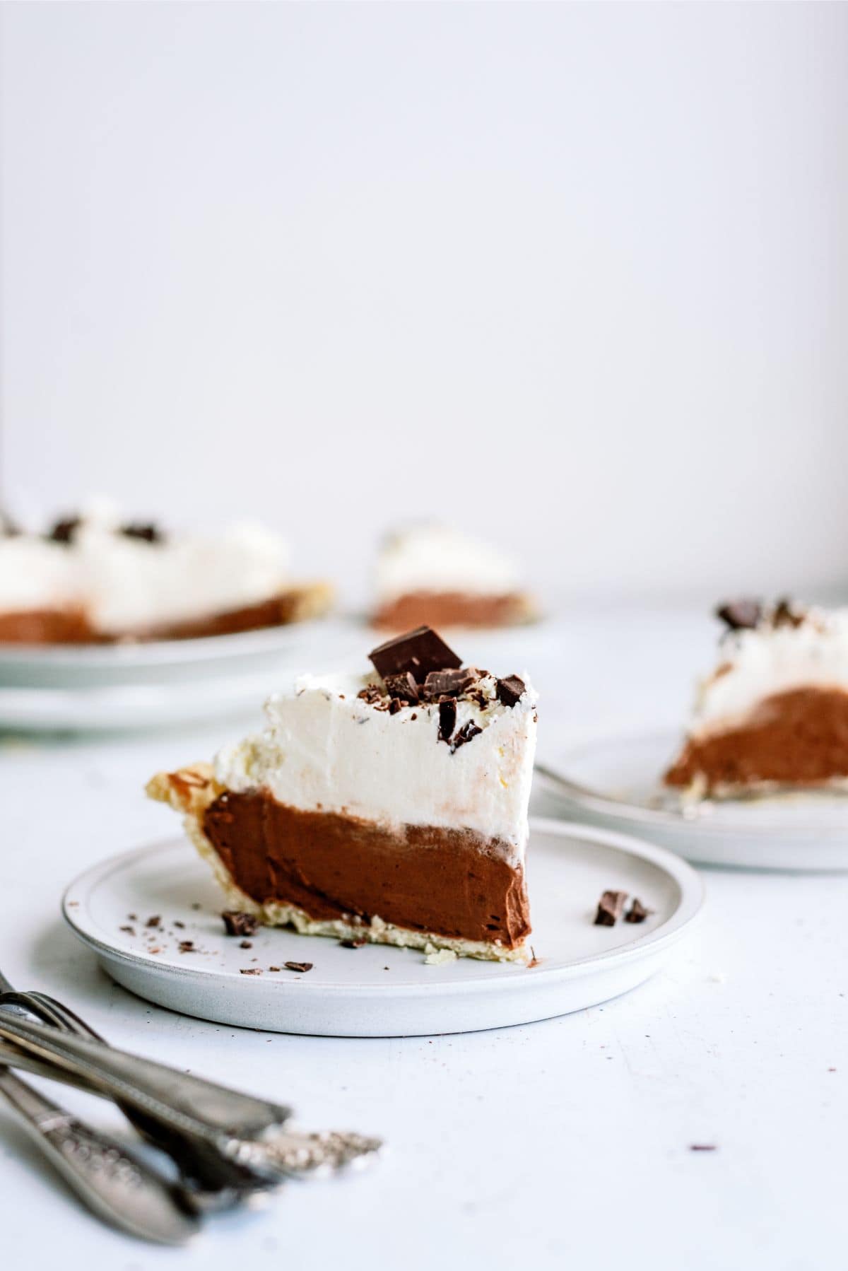 A slice of Chocolate Cream Pie on a plate. With the remaining pie in the background.