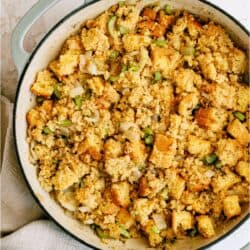 A large round pan filled with cornbread stuffing containing cubed bread, chopped celery, and onions, resting on a beige cloth.