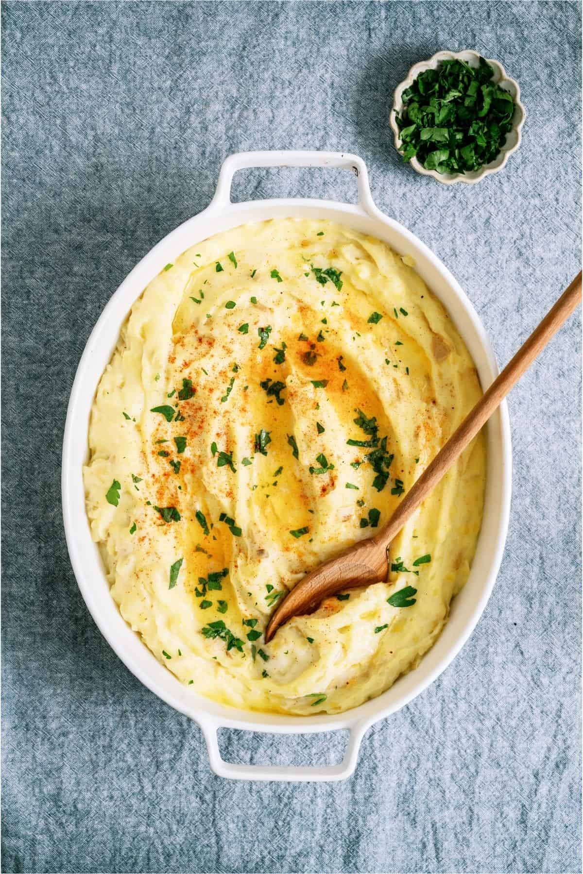 Make-Ahead Mashed Potatoes in a white casserole dish with a wooden spoon.