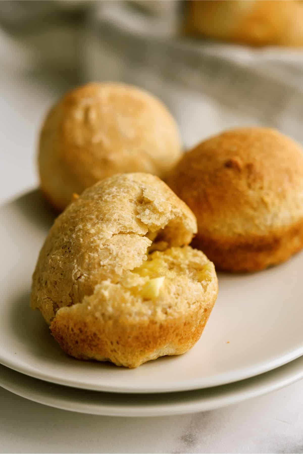 No Knead Honey Wheat Dinner Rolls  on a plate cut in half with butter spread on them