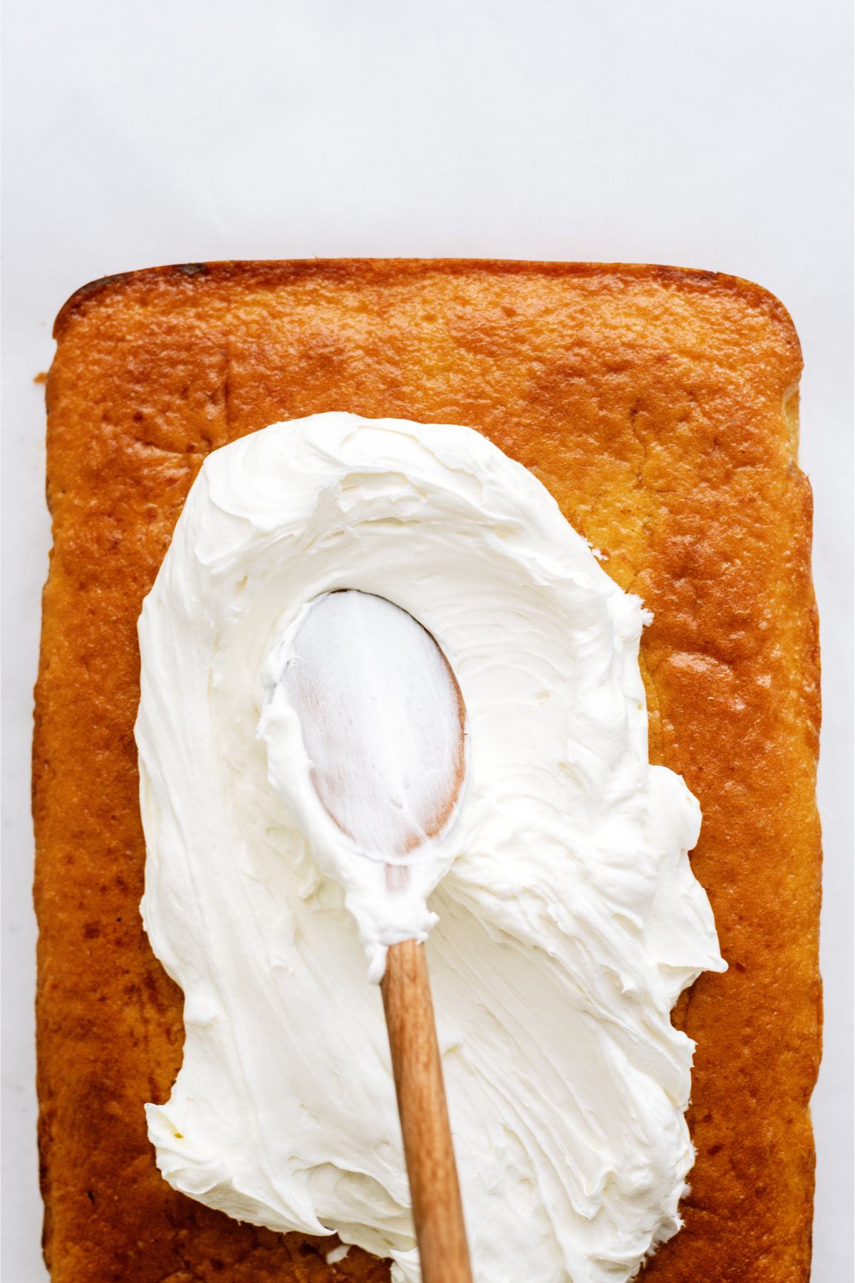 Spreading frosting on Pumpkin Layered Magic Cake with a wooden spoon