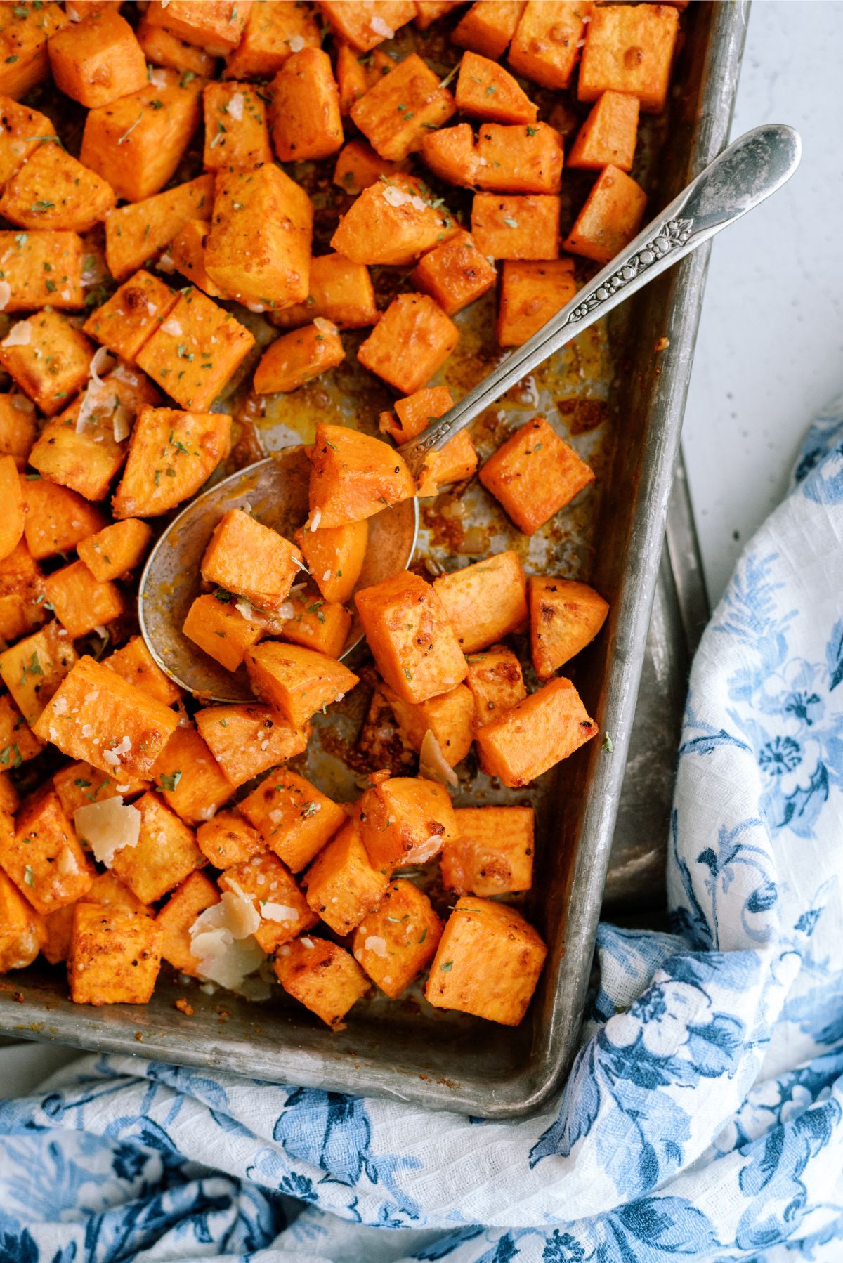 Roasted Parmesan Sweet Potatoes on a baking sheet with a serving spoon