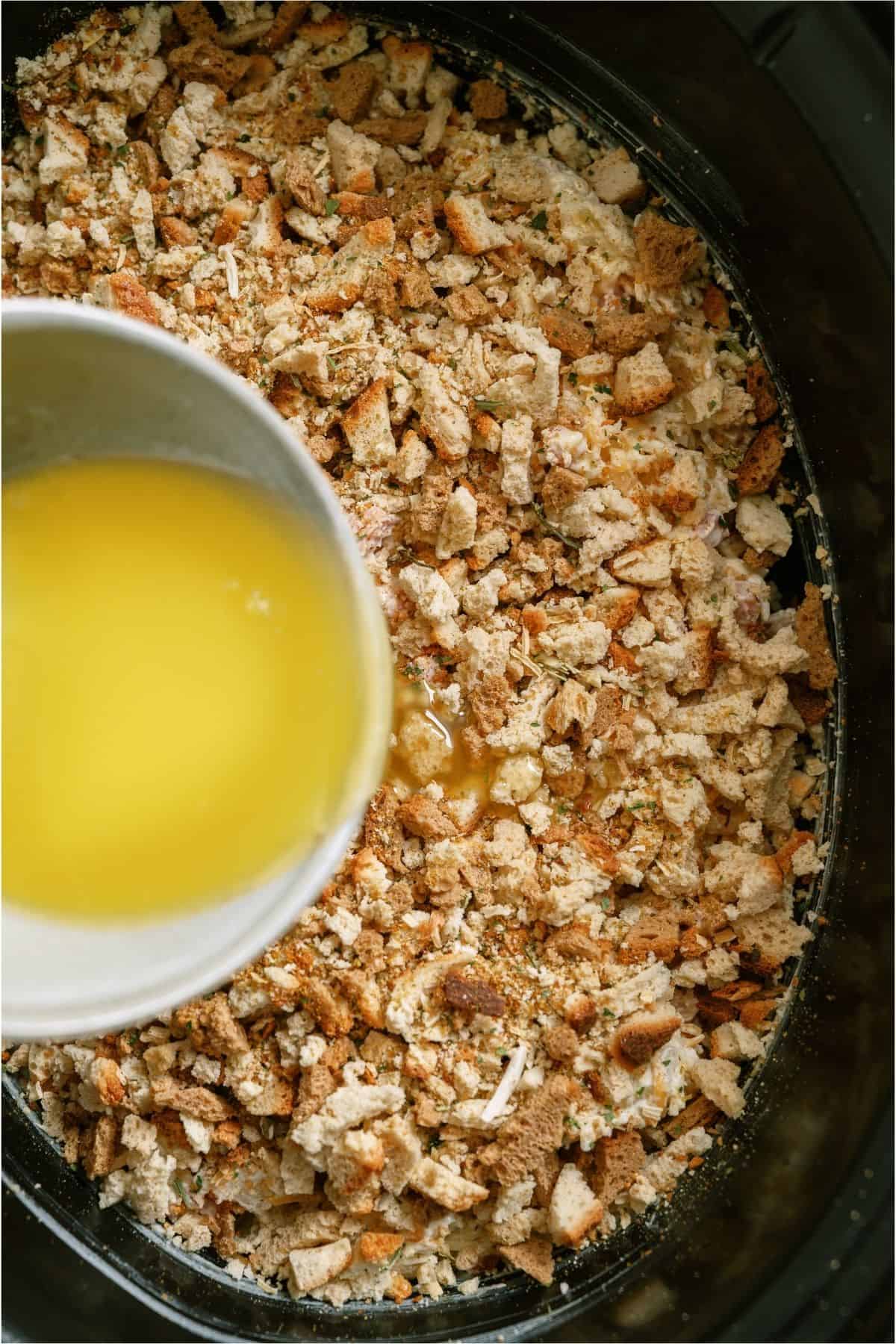 A layer of stuffing on top and a bowl of melted butter being poured on top.