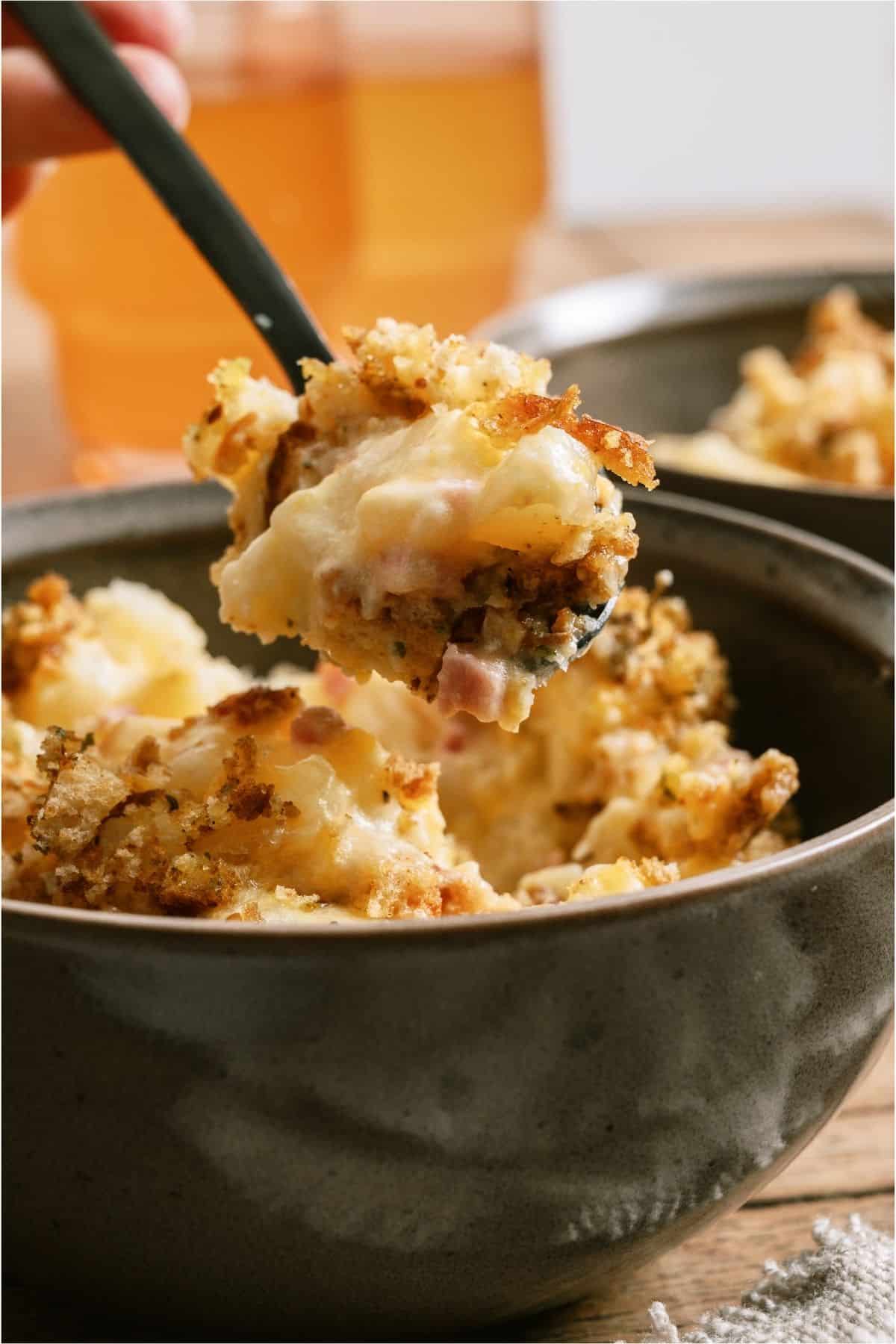 A fork lifting a bite of Slow Cooker Ham and Potato Casserole out of the bowl.