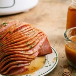 Slow Cooker Honey Baked Ham sliced on a plate with a slow cooker in the background.