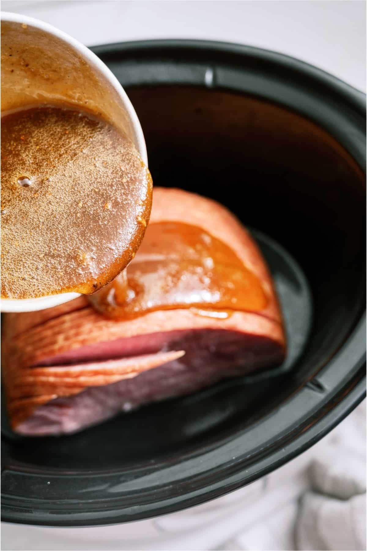 Pouring glaze on top of Slow Cooker Honey Baked Ham inside slow cooker.