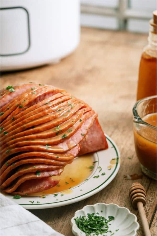 Slow Cooker Honey Baked Ham sliced on a plate with a slow cooker in the background.