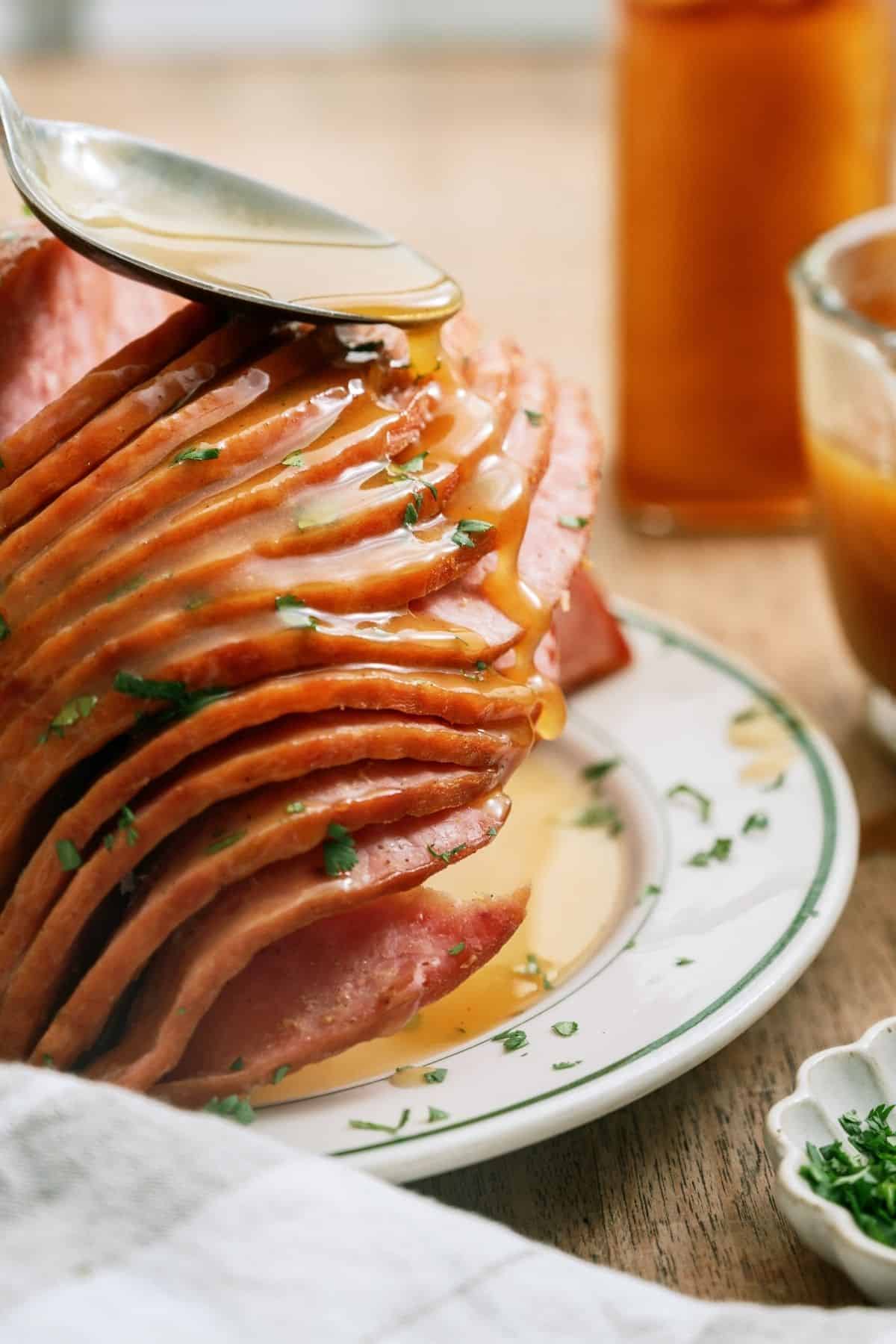 Spooning sauce on top of ham on a plate.