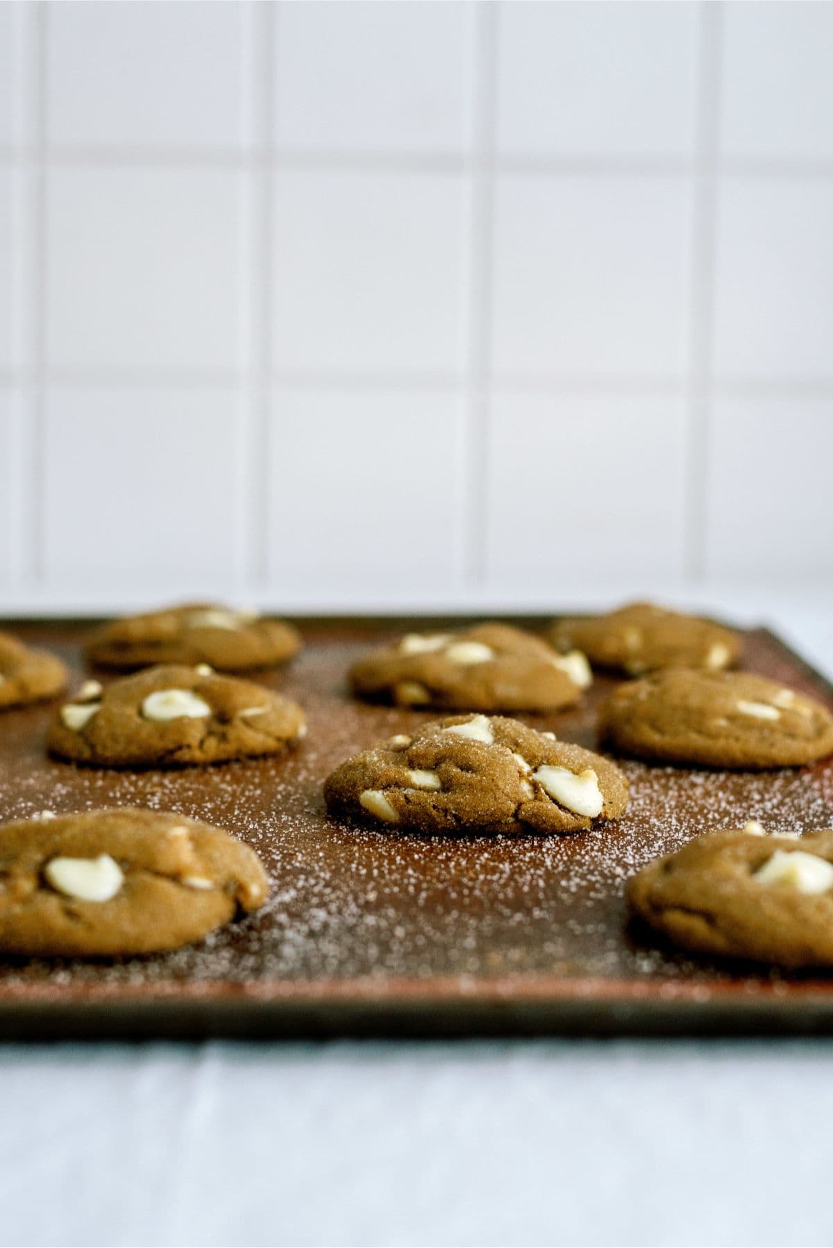 Side view of White Chocolate Chip Gingerbread Cookies on a baking sheet with sugar sprinkles all over the pan.