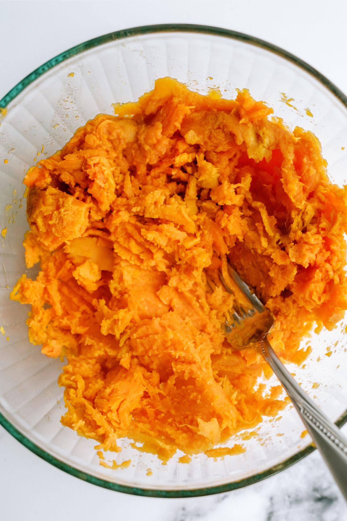 Sweet Potatoes mashed with a fork in a mixing bowl