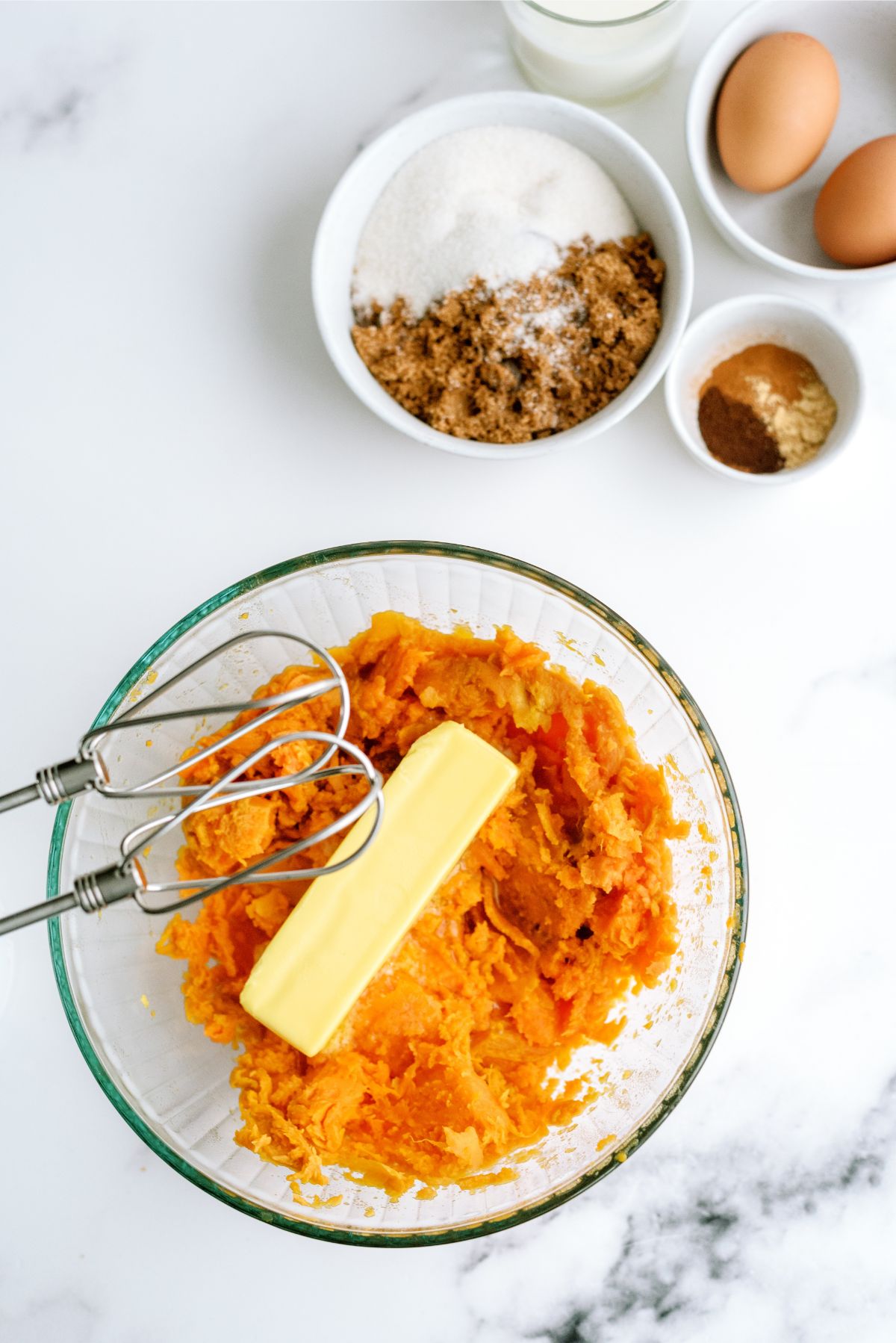 Mashed sweet potatoes in a mixing bowl with butter and a hand mixer