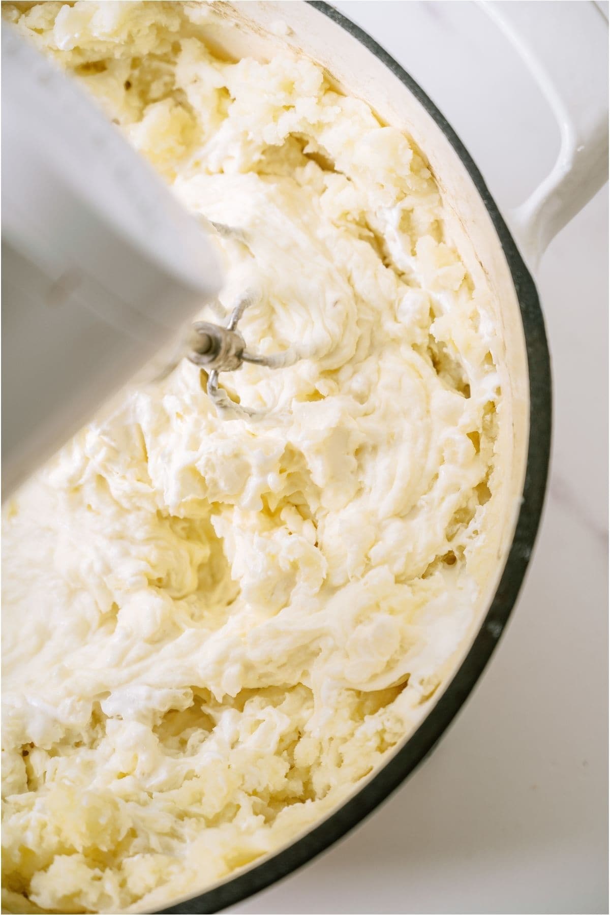 A bowl of potatoes in a glass mixing bowl mashed with electric beaters.