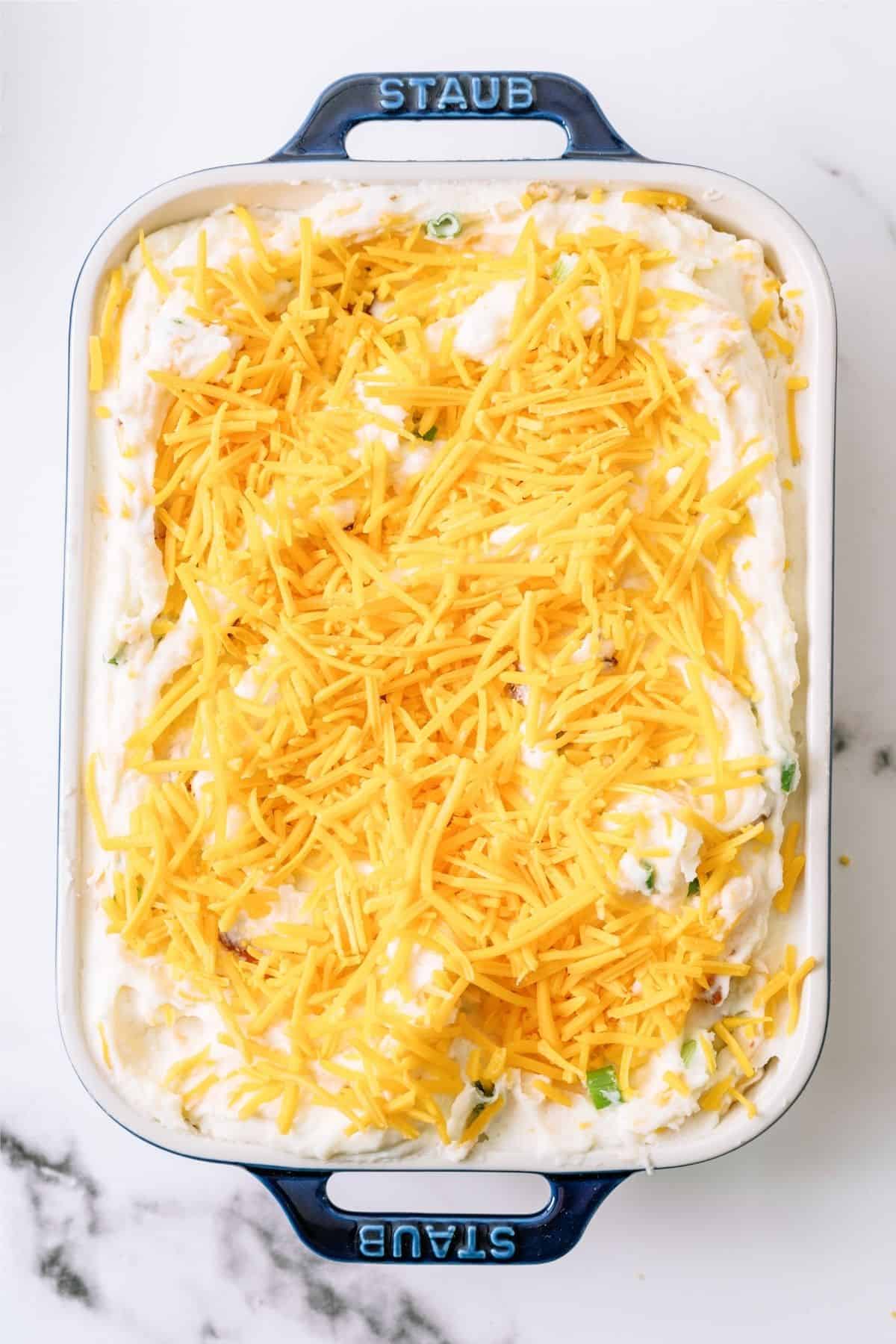 Shredded cheese on top of potato layer in baking dish.