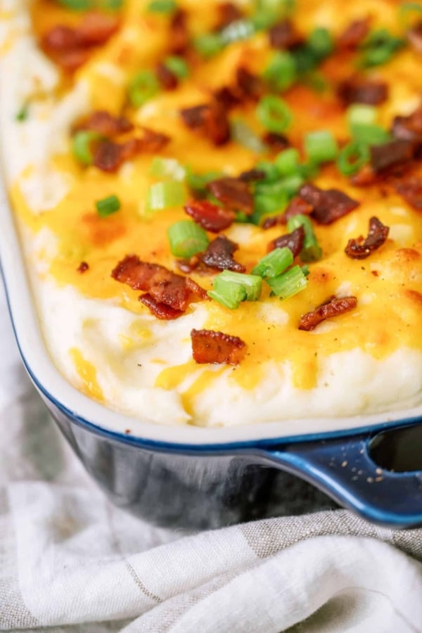 The corner of a baking dish of Twice Baked Potato Casserole topped with bacon and green onions.