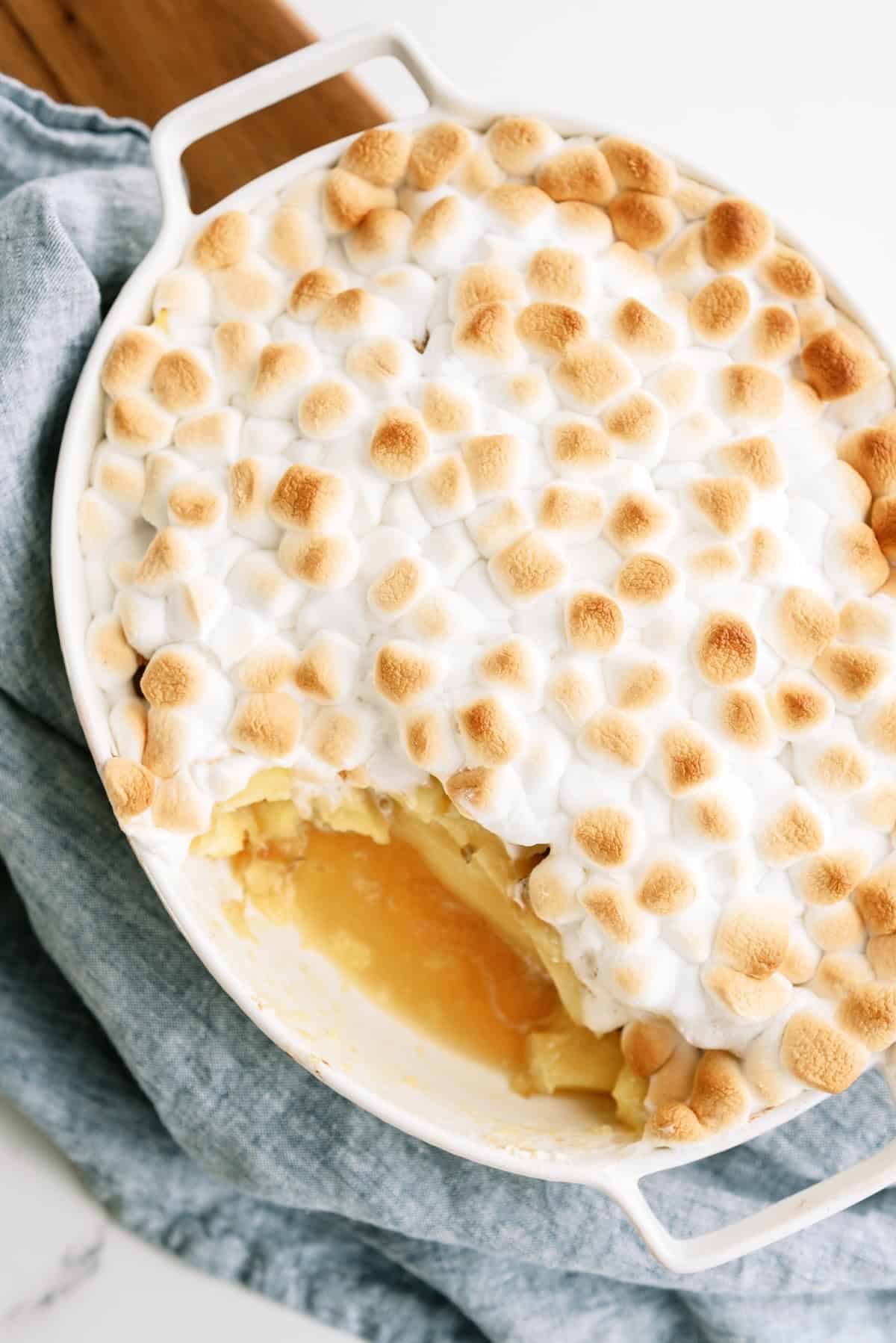 A baked casserole topped with toasted mini marshmallows, partially scooped to reveal a yellow filling underneath.